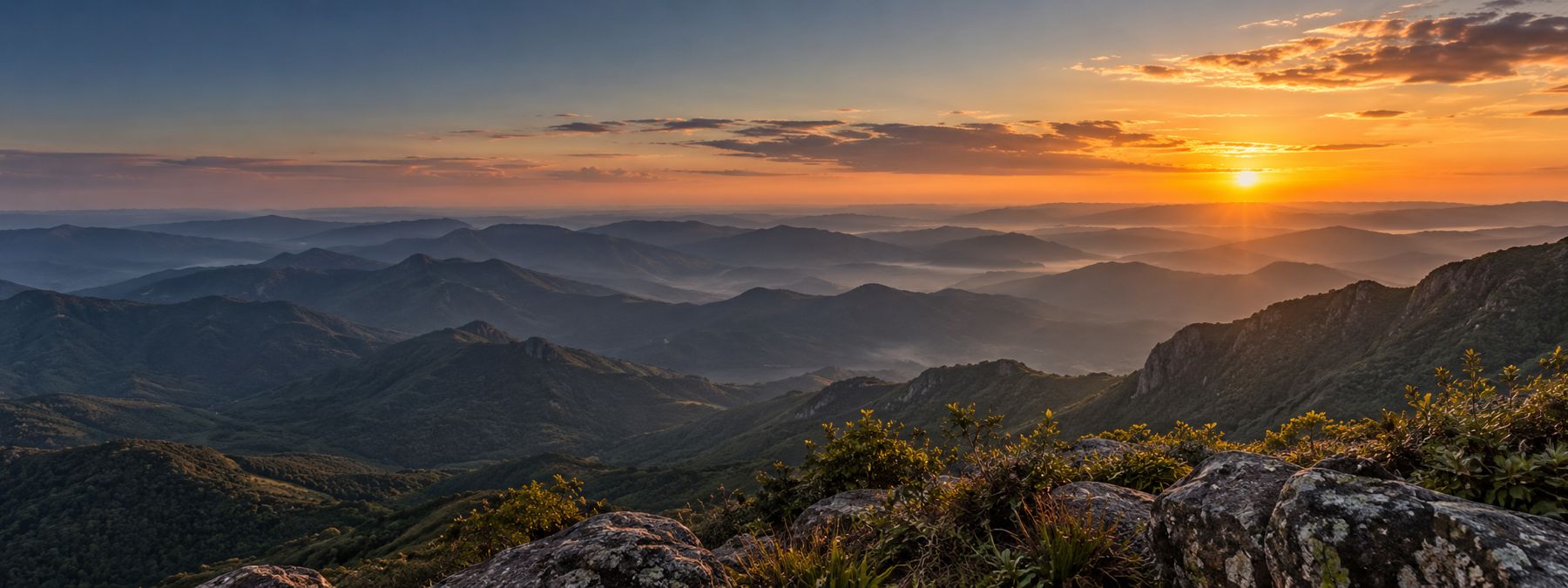 Nascer do sol sobre serras cobertas de mata, com névoa nos vales